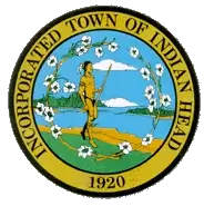Seal of the Incorporated Town of Indian Head, featuring a Native American figure holding a spear, surrounded by white flowers and water scenery, with “Incorporated Town of Indian Head” and “1920” around the border.