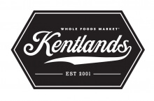 A black hexagonal logo for Whole Foods Market Kentlands, featuring "Kentlands" in large script and "EST 2001" below, with a curved underline and white lettering.