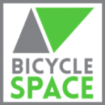 A square logo with a gray triangle and a green triangle above the words “BICYCLE SPACE,” with “BICYCLE” in gray and “SPACE” in green, all on a white background with a gray border.